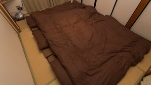 Una cama bien hecha con edredón marrón, una mesita de noche con lámpara y un calentador fijado a la pared.