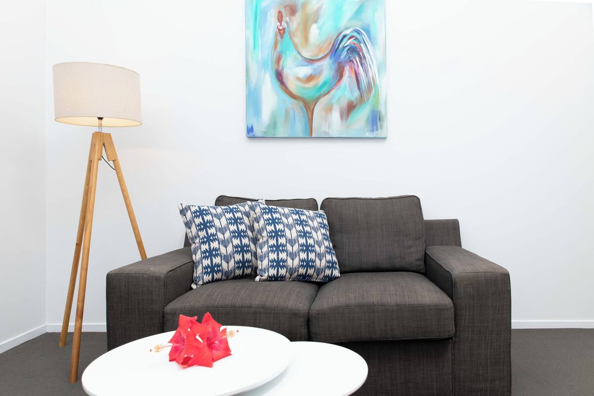 Ein modernes Wohnzimmer mit einem grauen Sofa, gemusterten Kissen, einem weißen Couchtisch und einer Stehlampe.