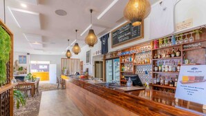 Una zona de bar con mostrador de madera, luces colgantes y estantes con botellas.