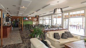 Un amplio vestíbulo de hotel con zona de comedor, mostrador de recepción y grandes ventanales con vistas al exterior.