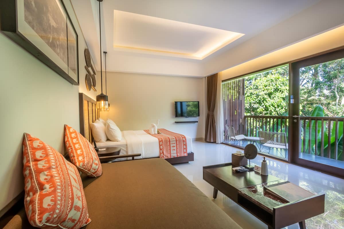 Quarto de hotel moderno com sofá, duas camas, televisão e varanda com vista para o verde.
