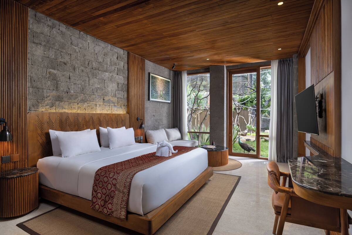 Quarto de hotel com uma cama grande, uma escrivaninha, uma televisão e vista para o exterior.