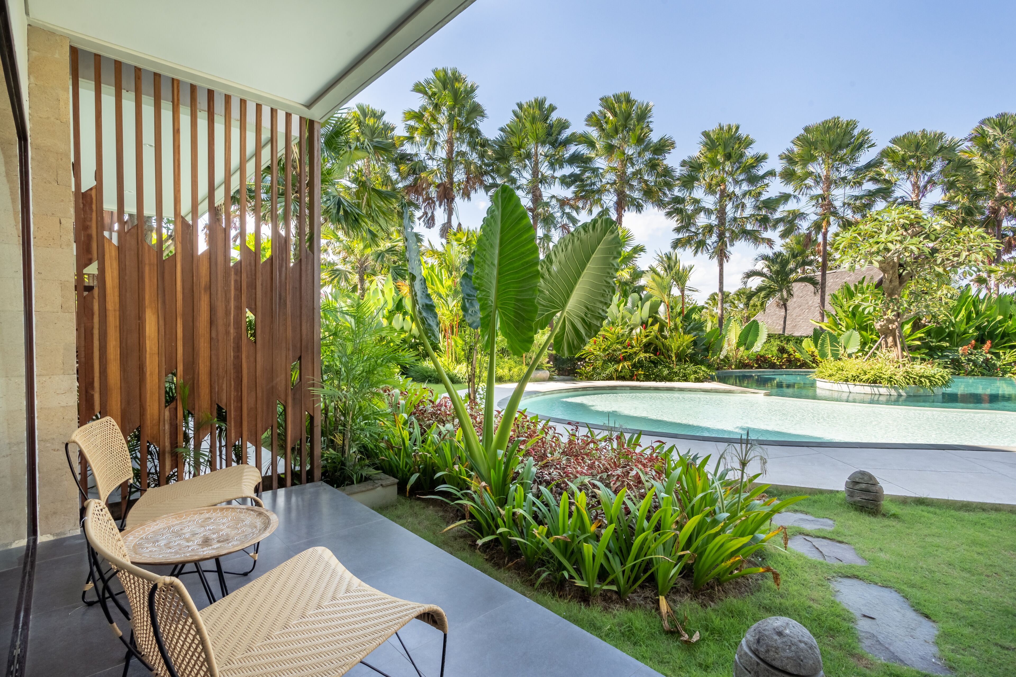 A patio with wicker furniture, a pool, and tropical plants.