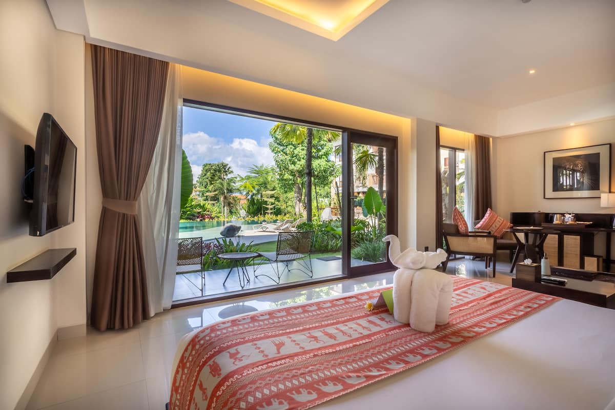 Quarto de hotel moderno com cama grande, televisão, escrivaninha e vista para a piscina e jardim.
