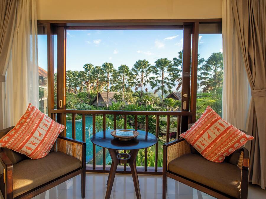 Un balcon avec deux fauteuils confortables, une petite table et une vue sur un paysage tropical, avec des palmiers et une piscine.
