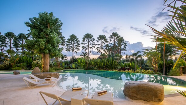 A poolside area with lounge chairs and a large rock. - Sanctoo Suites and Villas (Sukawati)