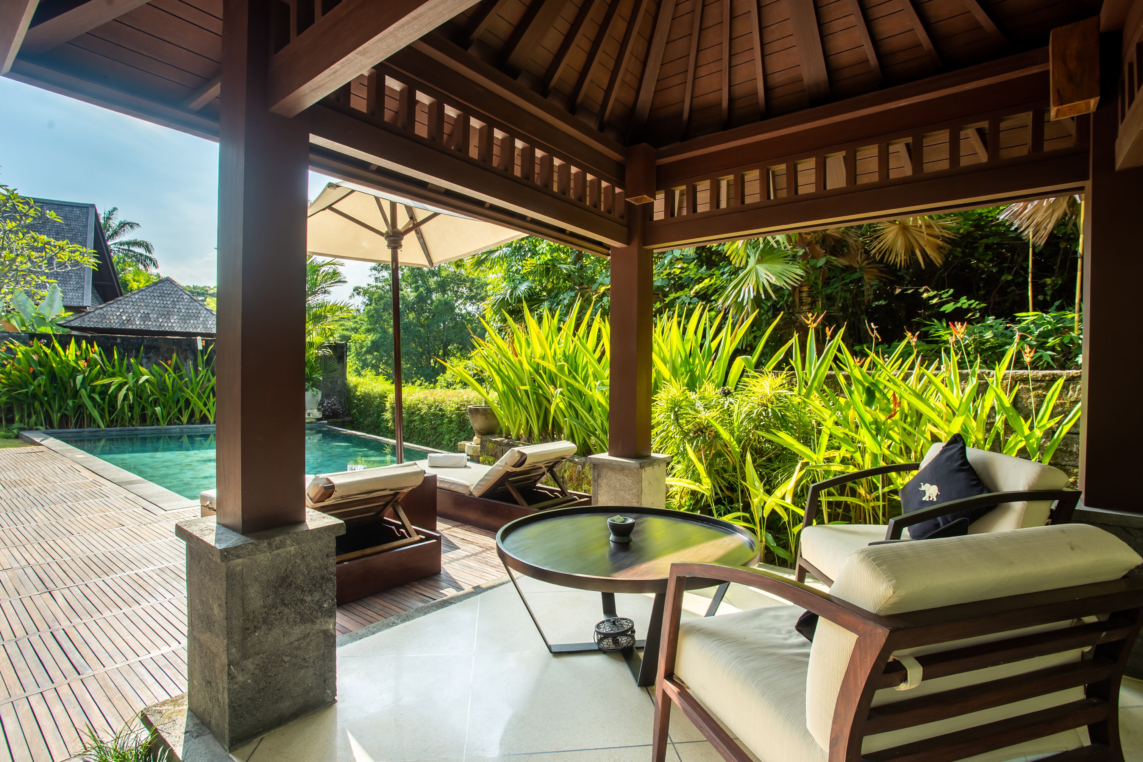 A covered outdoor seating area with a pool, lounge chairs, and a table.