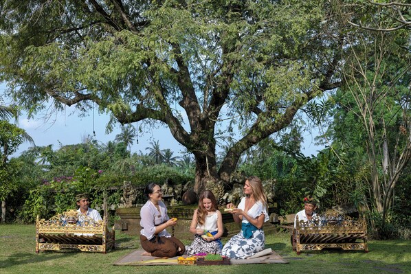 A group of people sitting on ornate benches under a large tree in a lush garden setting.