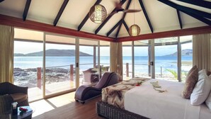 Une chambre avec un grand lit, une chaise longue et une vue sur la plage et la mer.