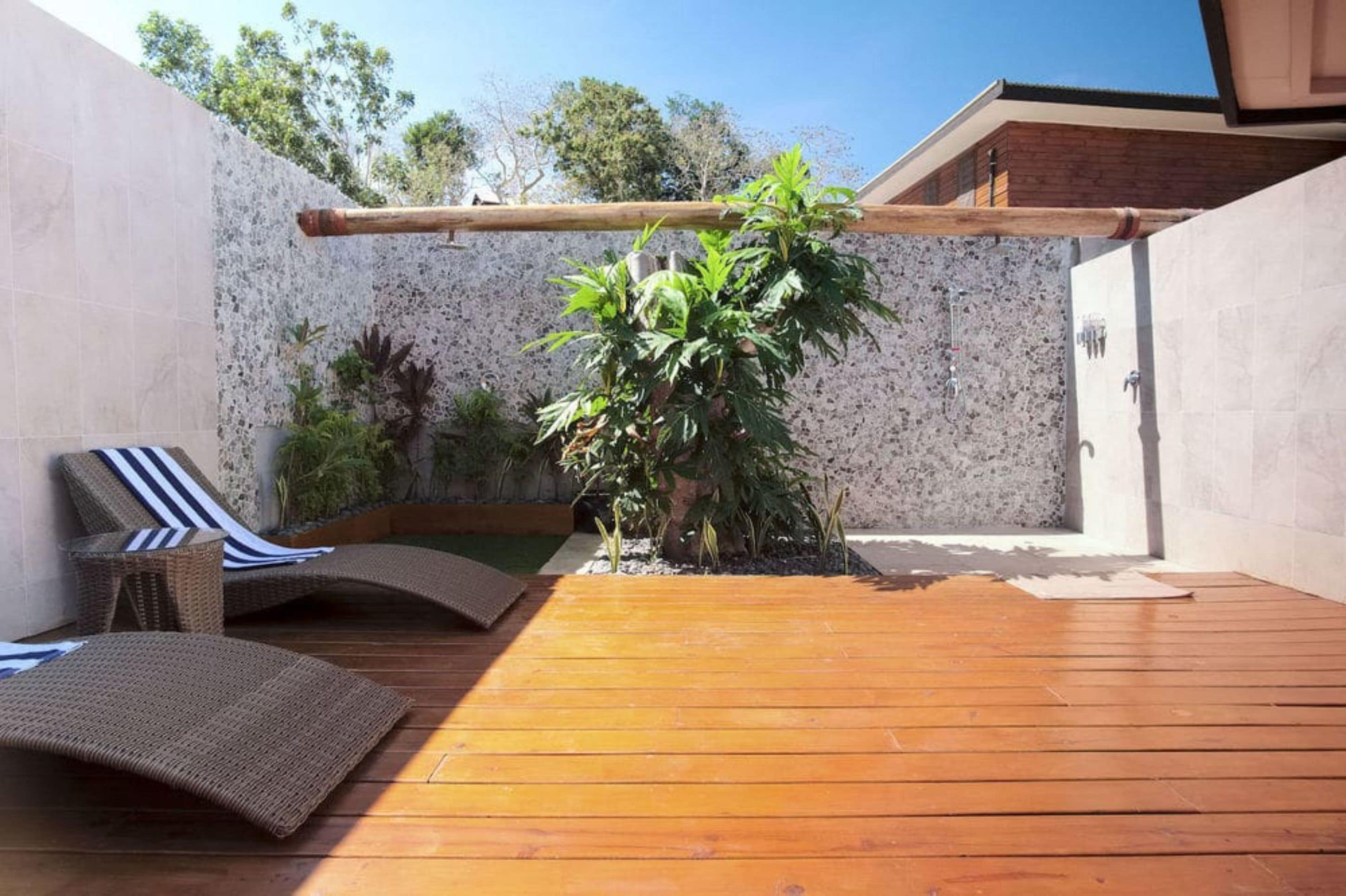 A wooden deck with a lounge chair and a small table, surrounded by plants and a stone wall.