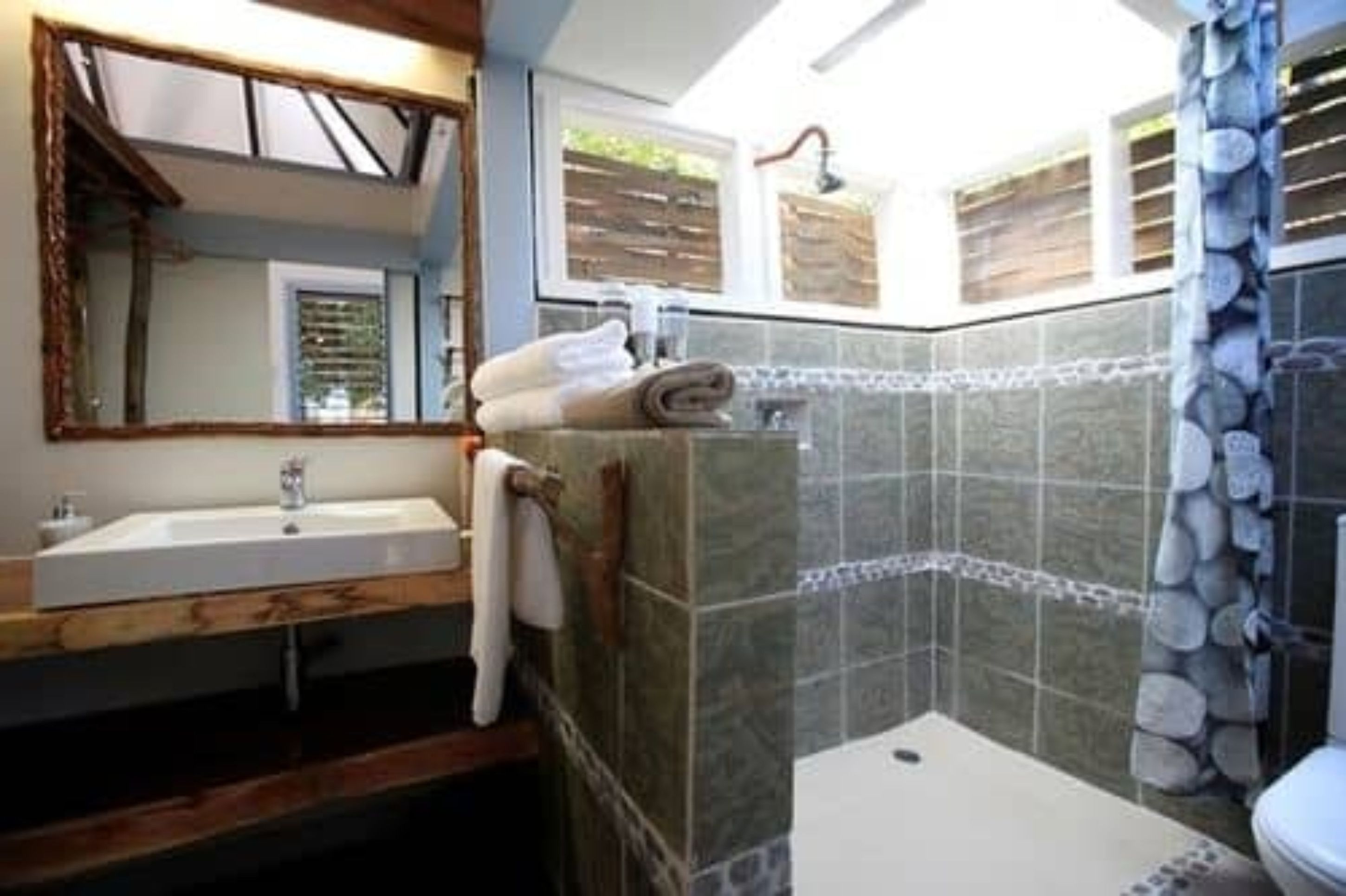 A bathroom with a wooden vanity, a large mirror, a shower with stone tiles, and a toilet.