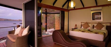 A bedroom with a bed, a chaise lounge, and a view of the sea.