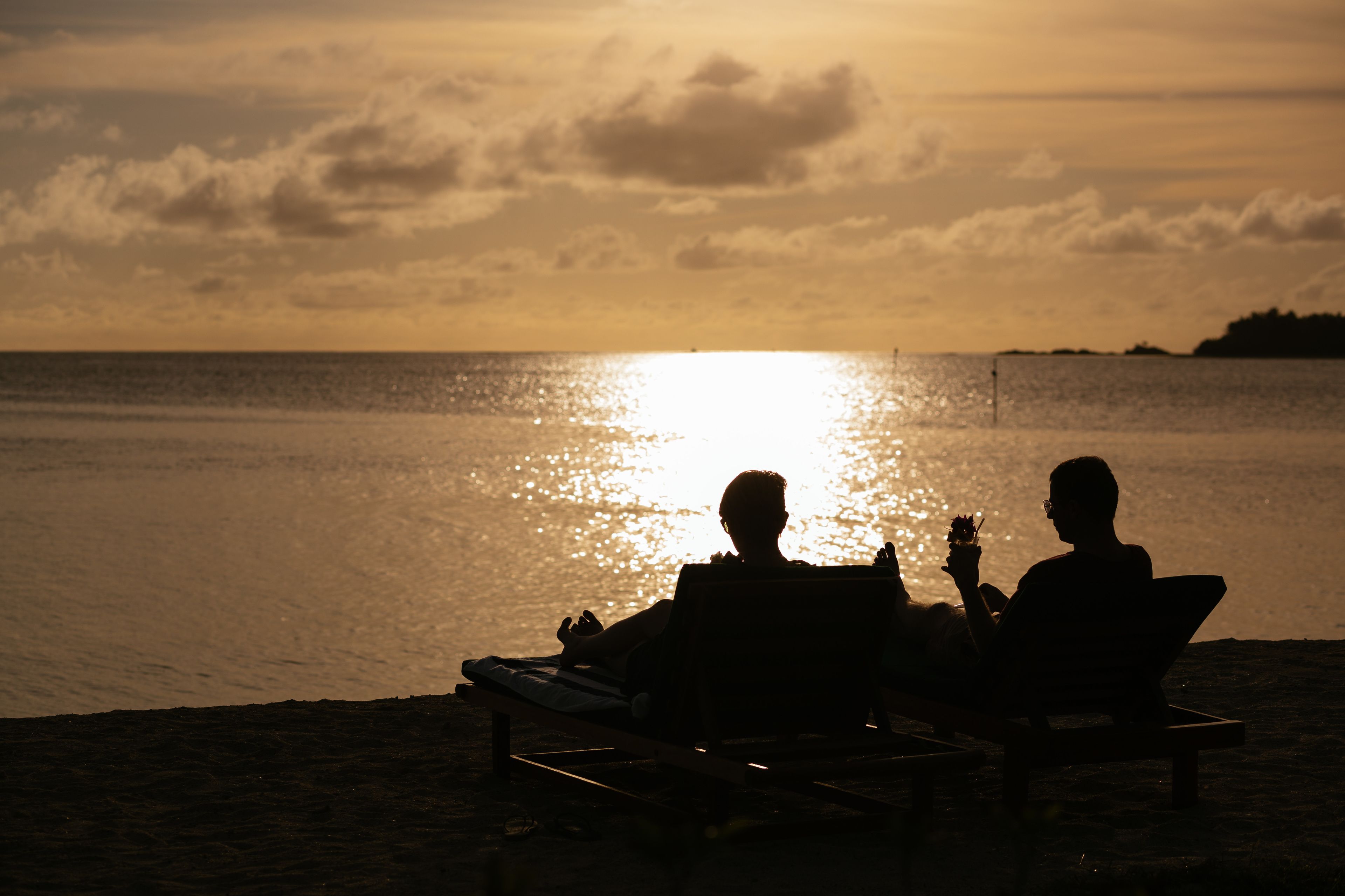 Two people sitting on beach chairs facing the ocean at sunset.