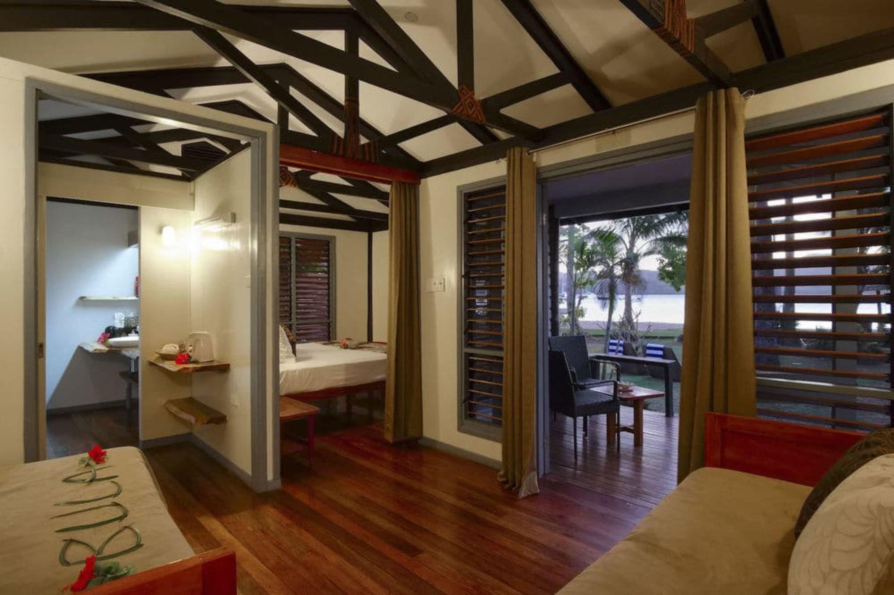 A room with a wooden floor, a bed, a desk, and a window with blinds.