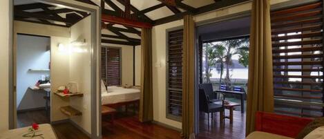 A room with a wooden floor, a bed, a desk, and a window with blinds.