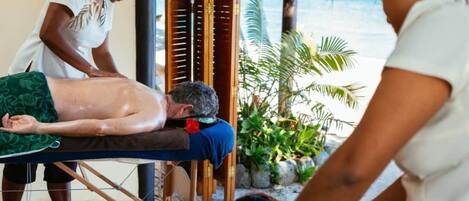 A massage therapy session in a room with a wooden floor, a massage table, and a view of the ocean.