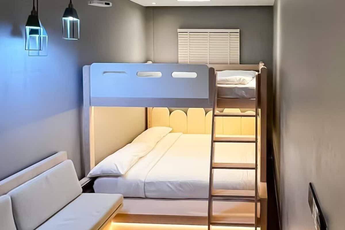 Una cama litera con escalera, un sofá e iluminación colgante en una habitación con techo inclinado y luces empotradas.