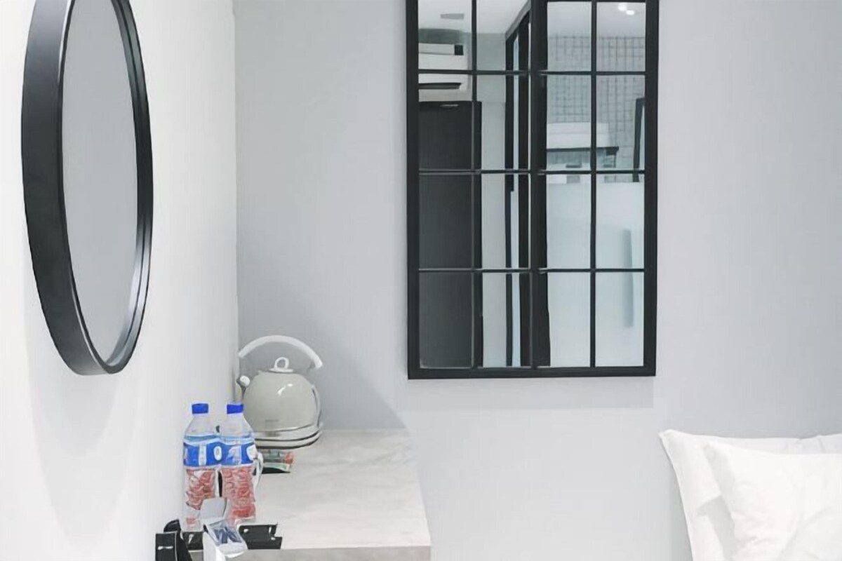 A modern bathroom with a large mirror, a kettle, and bottled water on the counter.