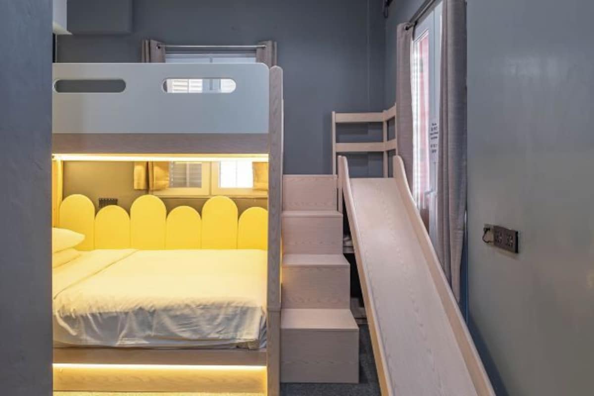 A compact, well-lit room with a bunk bed, a small desk, and a window with curtains.