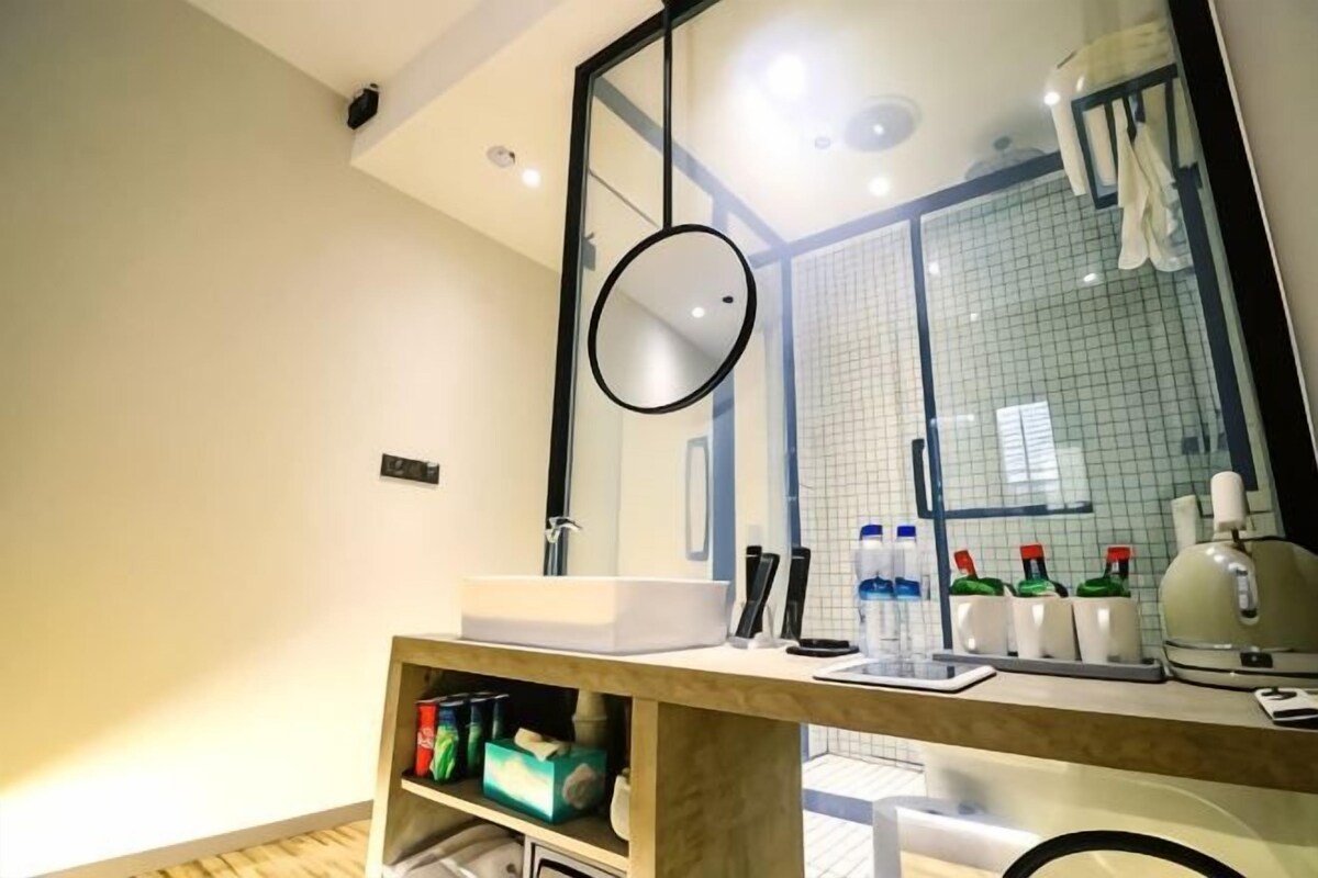A modern bathroom with a large mirror, a sink, and a shelf with toiletries.
