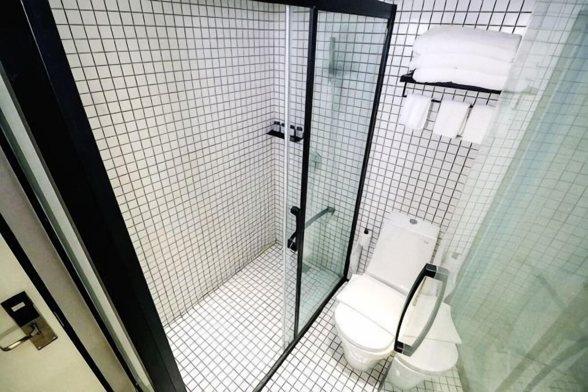 A tiled bathroom with a glass shower enclosure, a toilet, and a towel rack.