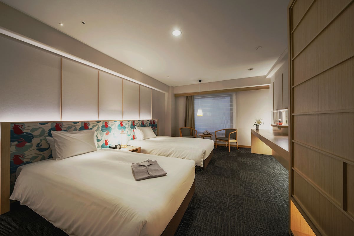A hotel room with two beds, a desk, and a chair.