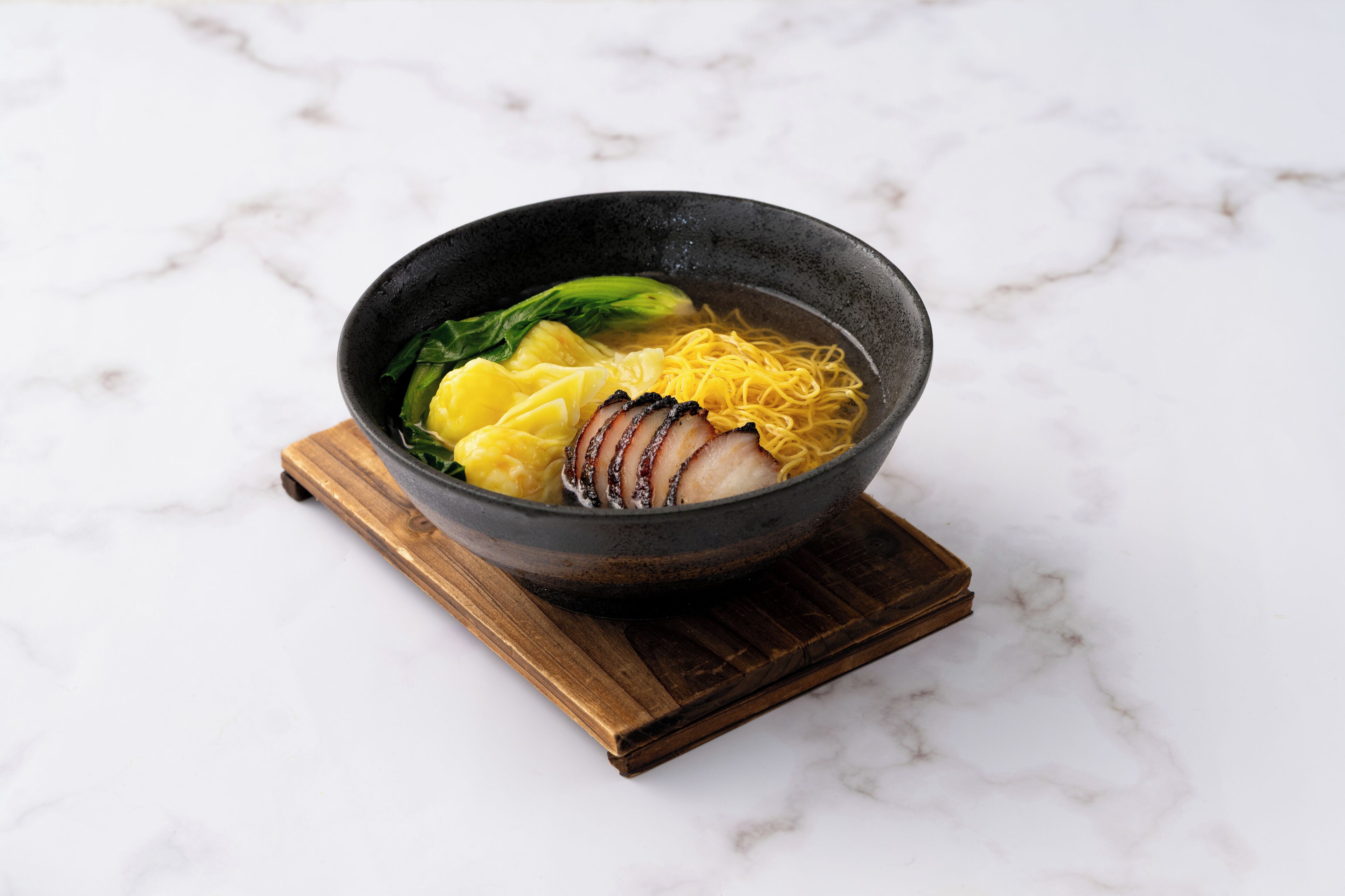 Un bol de ramen contenant des nouilles, des tranches de viande et du chou chinois, posé sur un dessous de verre en bois.