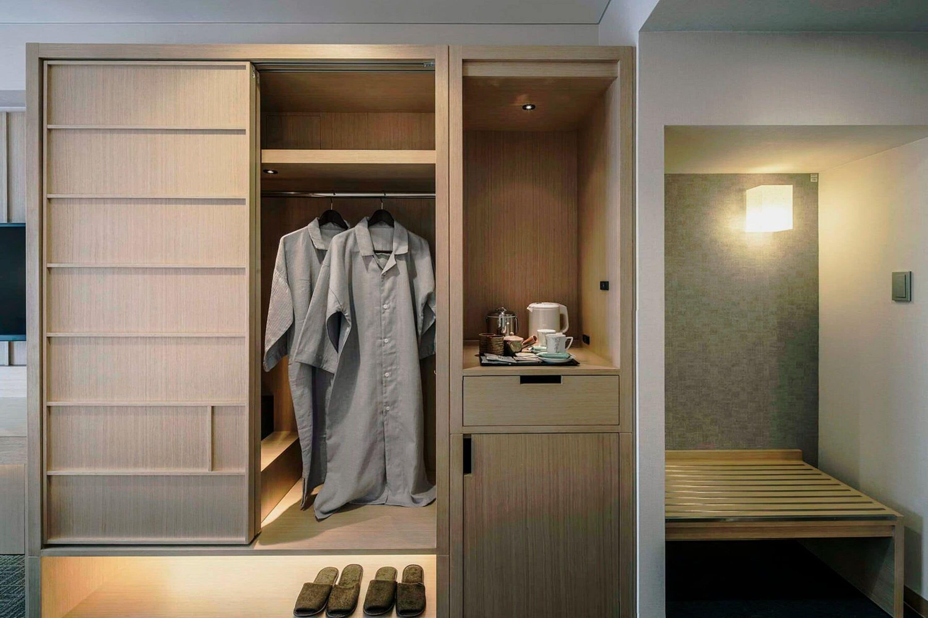 A walk-in closet with hanging clothes, a small table with a coffee maker, and a bench.