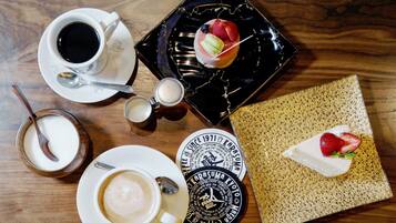 Une table avec une tasse de café, une assiette de nourriture, un petit bol de crème, une cuillère et deux sous-verres avec du texte.