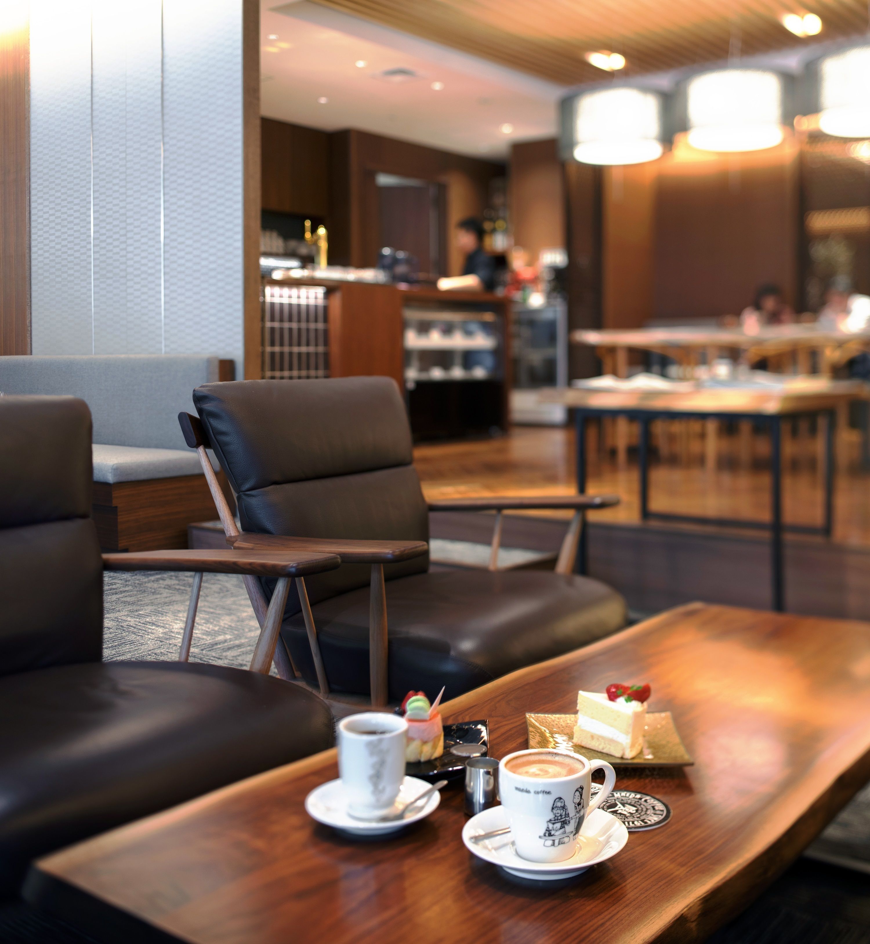 A modern cafe with leather seating, a wooden table with a cup of coffee and a cake, and a visible menu board in the background.
