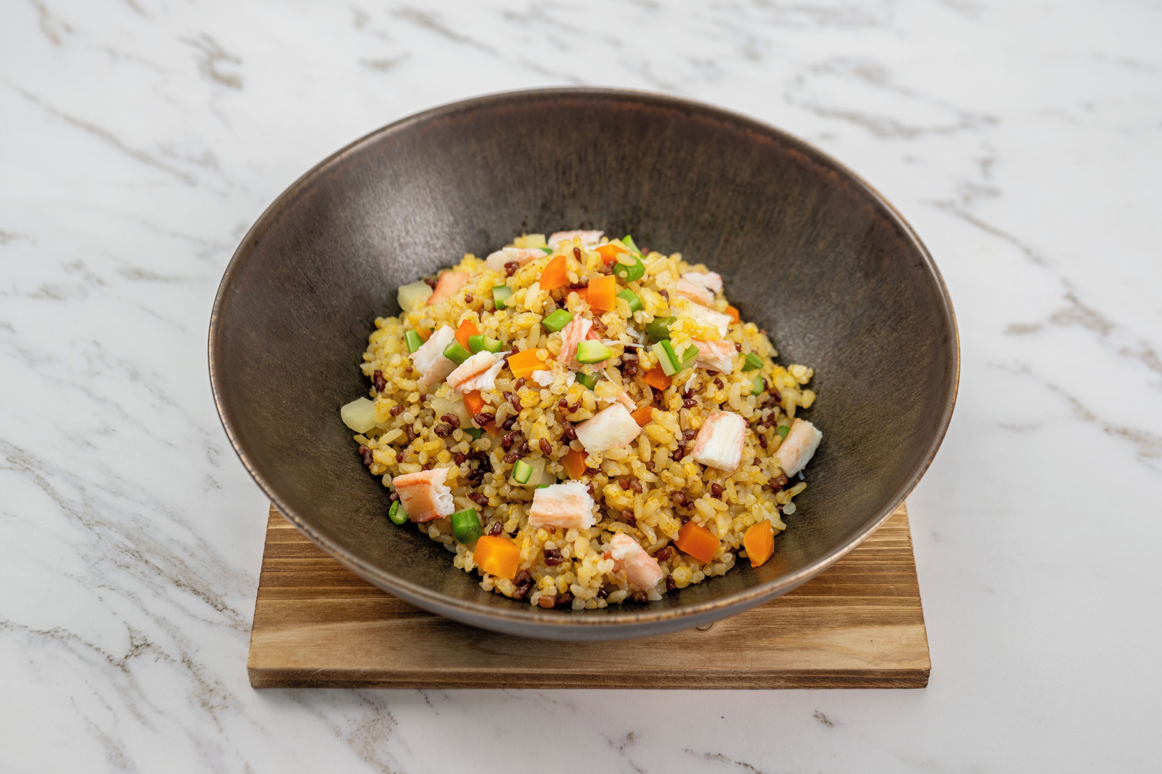A bowl of rice with vegetables and meat on a wooden board.