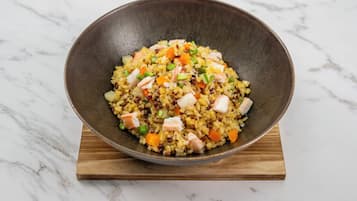 A bowl of rice with vegetables and meat on a wooden board.