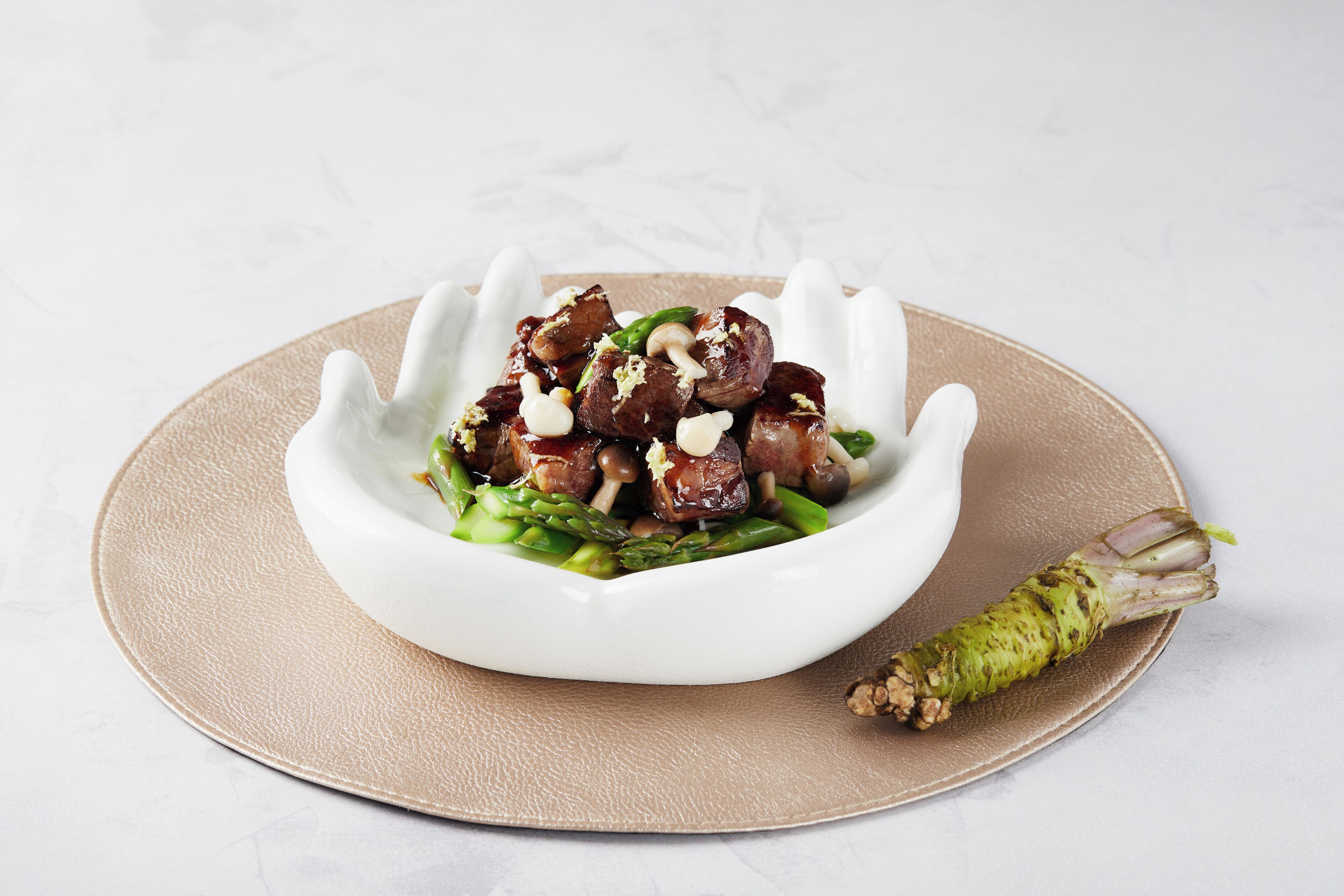 A white bowl with a unique design, containing a dish with meat and vegetables, on a beige plate.