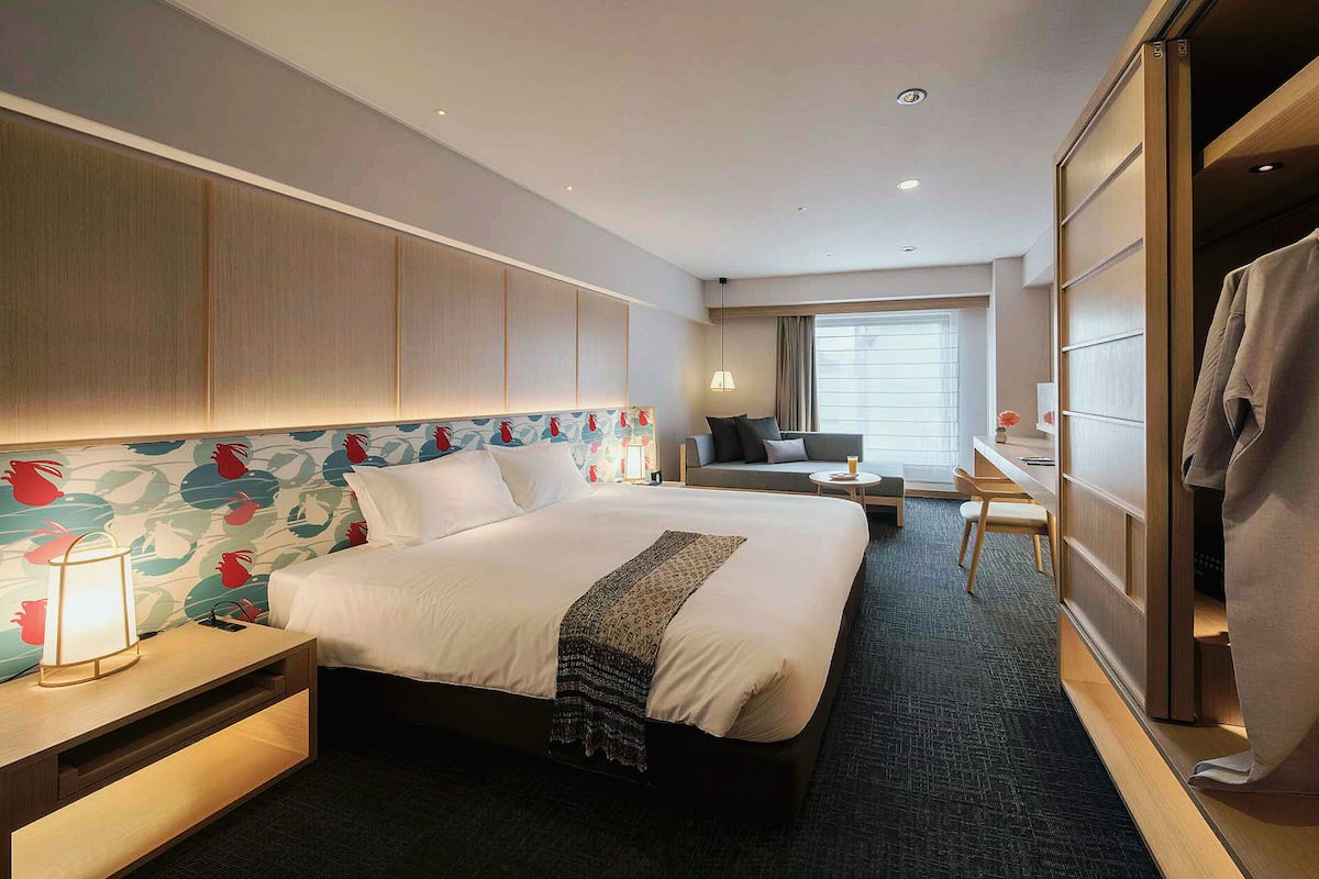 A hotel room with a large bed, a desk, a chair, a wardrobe, and a window with curtains.