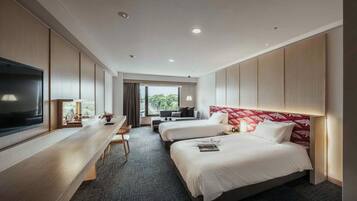 Habitación de hotel con dos camas, un escritorio, un televisor y vistas al exterior.