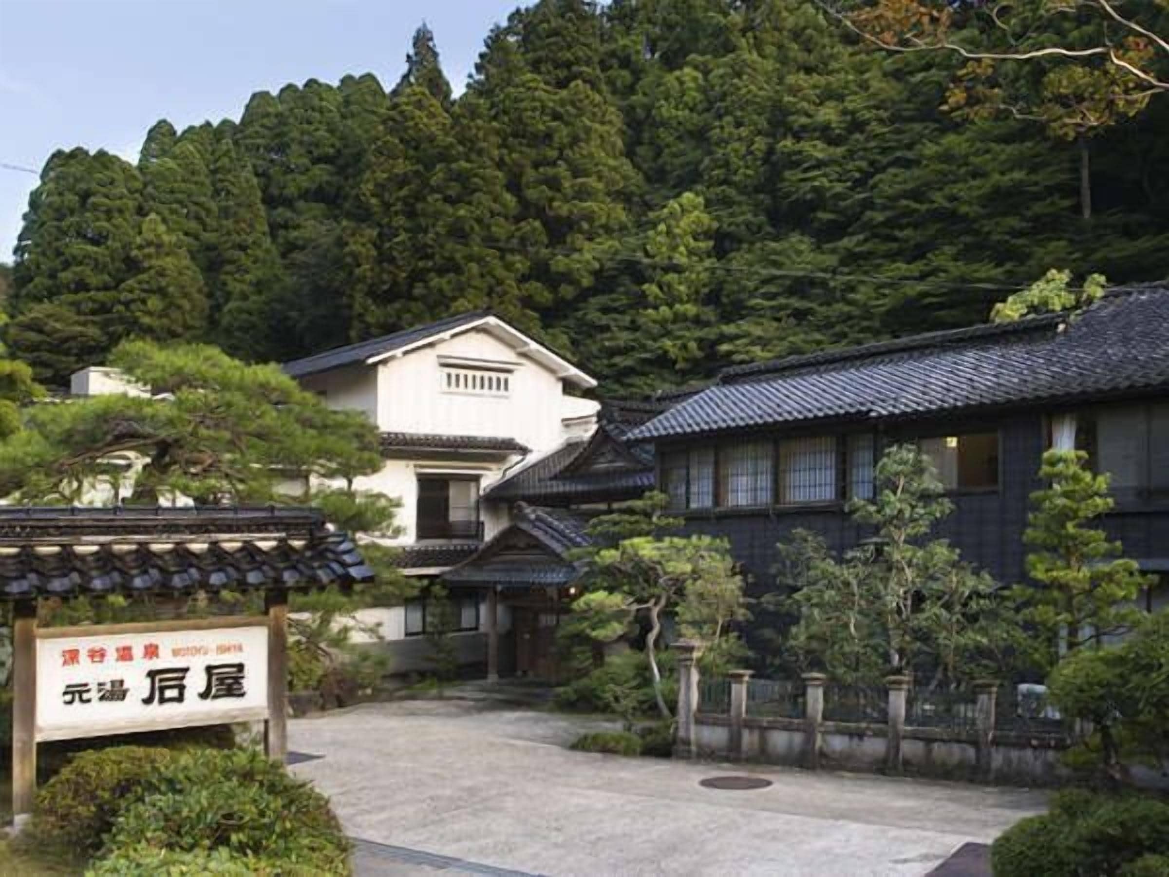 A traditional Japanese building with a tiled roof, surrounded by lush greenery and a stone pathway.