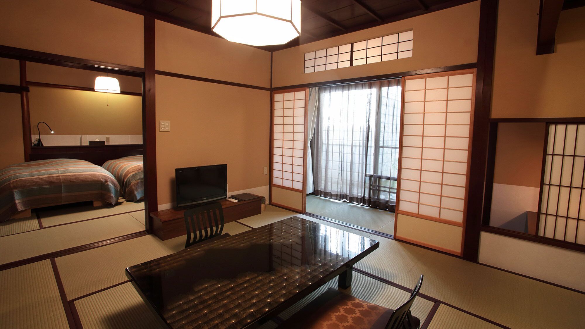 Ein traditioneller japanischer Raum mit Tatami-Bodenbelag, einem niedrigen Tisch mit Kissen, einem Fernseher und einer verschiebbaren Shoji-Schirmwand.