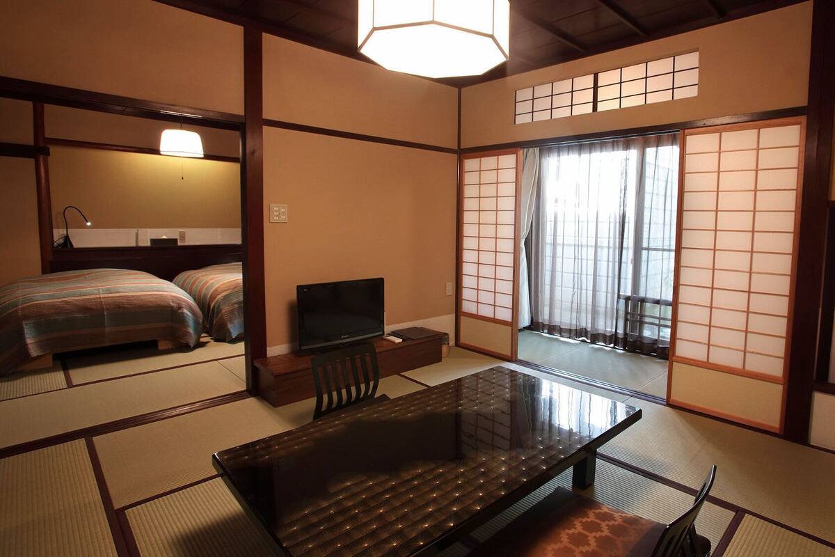 Une pièce de style japonais traditionnel, avec un sol recouvert de tatamis, une petite table basse avec des coussins, un téléviseur et un paravent coulissant de type shoji.