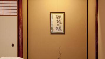 Um quarto japonês tradicional com tatames, uma mesa baixa, uma obra de caligrafia emoldurada e um pequeno vaso com um galho.