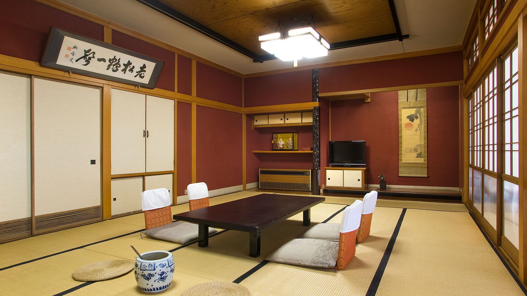 Une pièce de style japonais traditionnel, avec un sol recouvert de tatamis, une table basse, des coussins, un téléviseur et une porte coulissante.