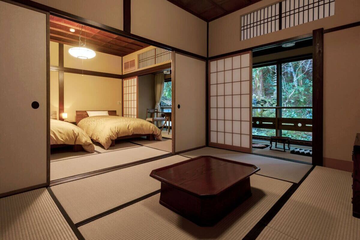 Une pièce de style japonais traditionnel, avec un sol recouvert de tatamis, une petite table en bois et un lit équipé d’un futon.