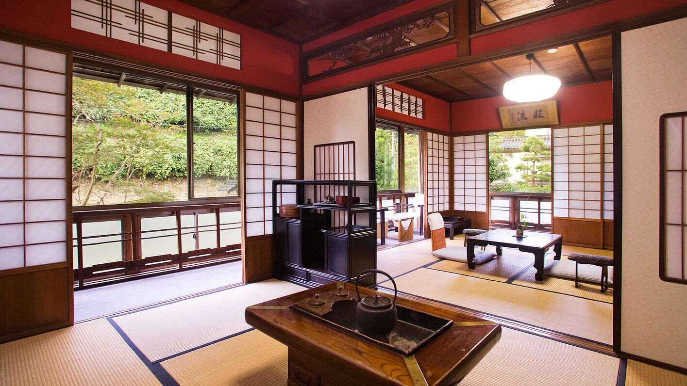 Une pièce de style japonais traditionnel, avec un sol recouvert de tatamis, des portes coulissantes et un service à thé posé sur une table en bois.