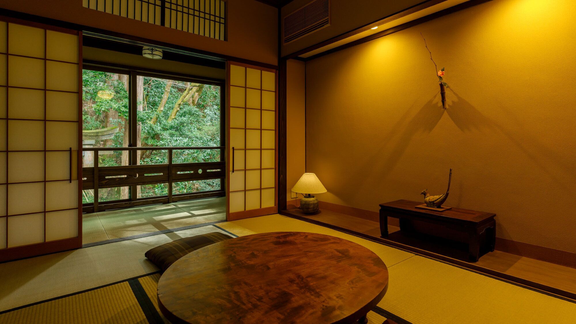 Une pièce de style japonais traditionnel, avec un sol recouvert de tatamis, une table basse, une lampe et une petite table ornée d’un objet décoratif.