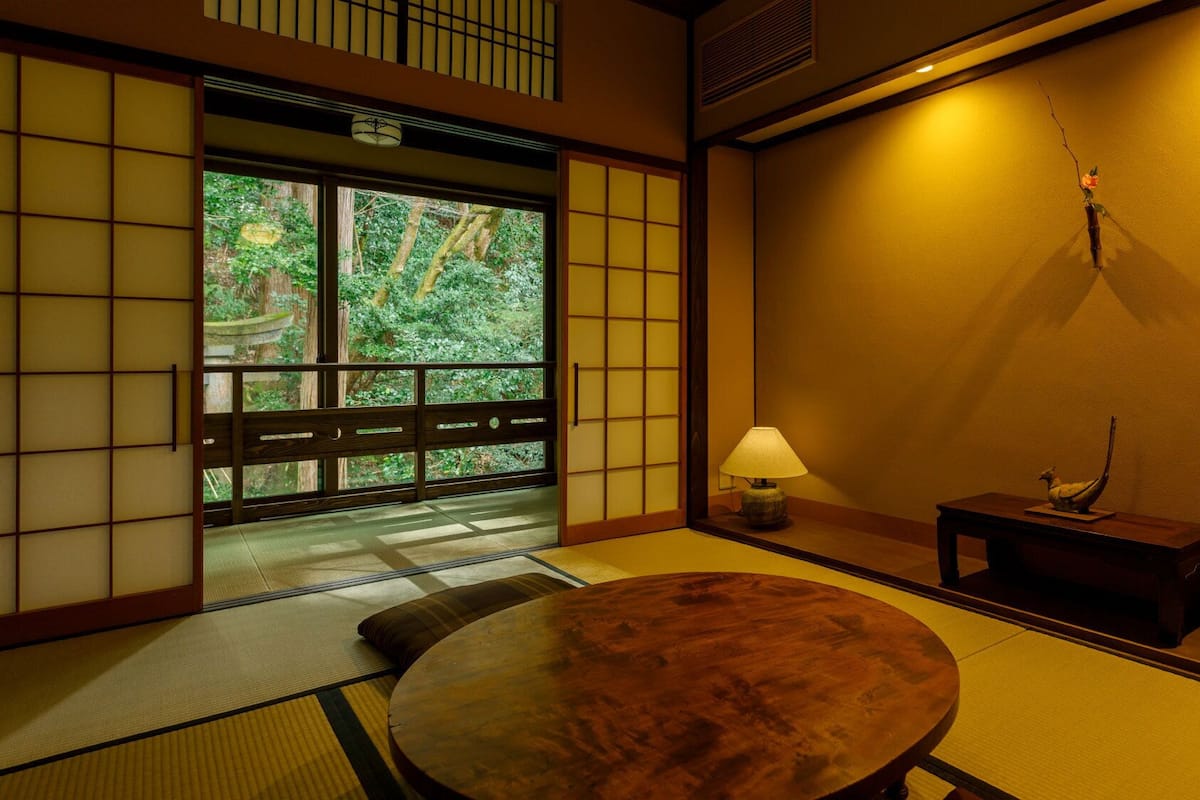 Una habitación japonesa tradicional con suelo de tatami, una mesita baja, una lámpara y una pequeña mesa con un objeto decorativo.