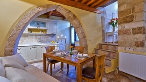 A cozy dining area with a wooden table set for four, a stone archway, and a kitchen in the background. - Kores Boutique Houses (Chania)