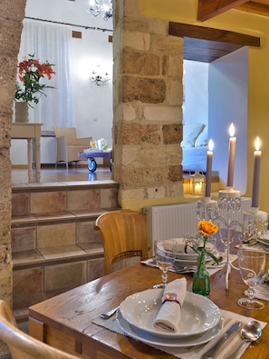 Uma sala de jantar com uma mesa de madeira posta para dois, um vaso com uma rosa amarela e velas sobre a mesa.