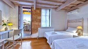 A bedroom with two beds, a wooden ceiling, a brick wall, and a view of an outdoor patio. - Kores Boutique Houses (Chania)