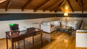 Une chambre à coucher confortable, aménagée en mezzanine, avec un plafond en bois, un canapé blanc, une table basse en verre et un bureau avec un ordinateur portable.