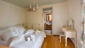Une chambre à coucher comprenant un lit, une table de chevet, une commode, un miroir et une porte donnant sur une salle de bain.