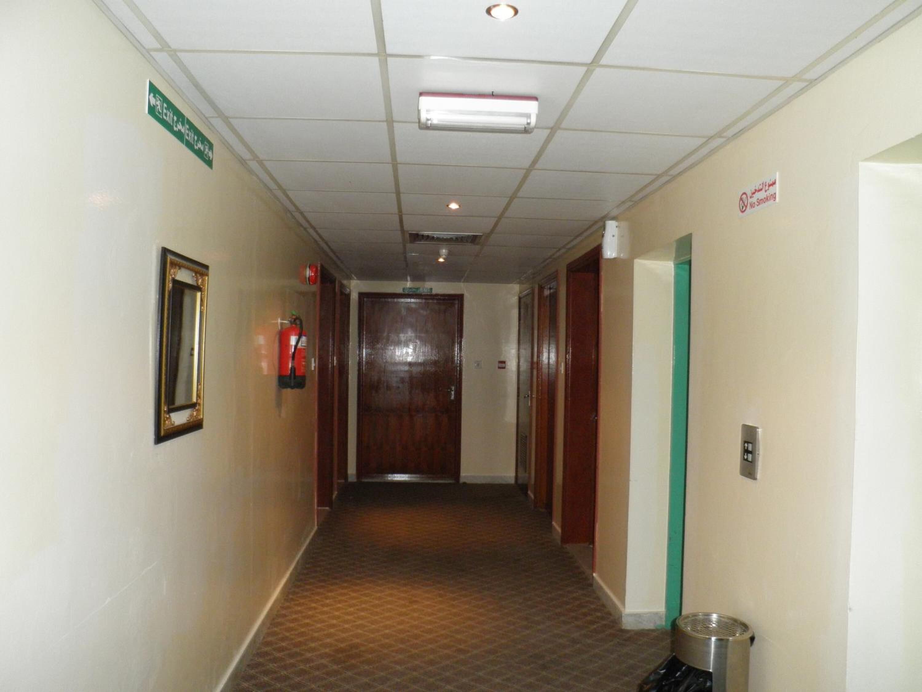 A hotel hallway with a fire extinguisher, a no smoking sign, and an exit sign.